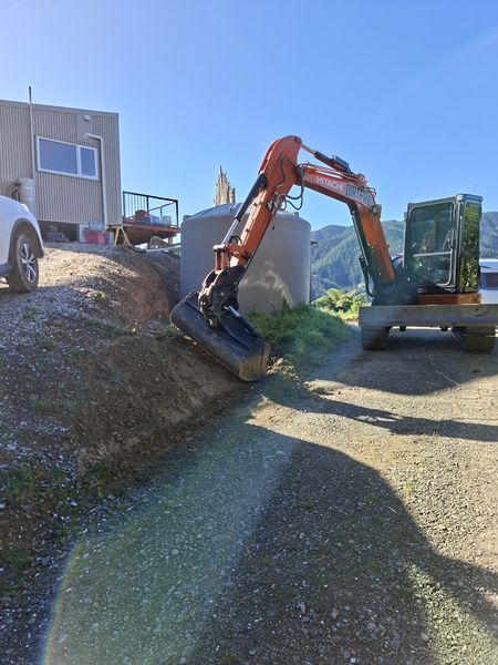 Hitachi excavator trimming a batter beside the water tank and gravel driveway, Mahau Sound