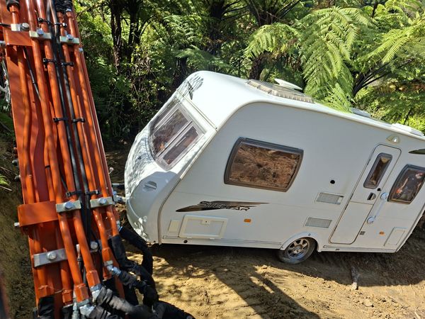 Excavator boom beside the caravan as it is dragged up the steep track through the bush