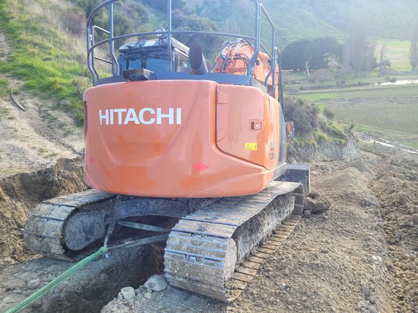 Excavator working on steep hillside drainage with pipe visible