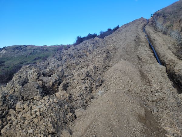 Completed hillside cut with excavator and truck on steep site overlooking vineyards